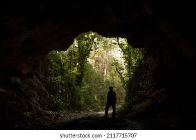 A male speleologist with a helmet exiting the dark cave after studying it