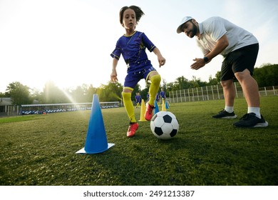 Male sport coach guiding young player through dribbling drill, encouraging and commentating. Focus and concentration. Concept of sport, childhood, education, achievement, active lifestyle - Powered by Shutterstock