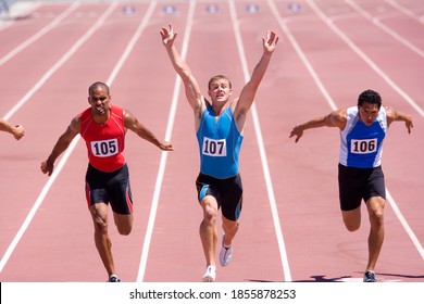 Male sprinter raising his arms in victory with his colleagues behind him on a bright, sunny day at the track - Powered by Shutterstock