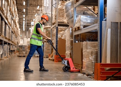 male staff worker in warehouse uses hand pallet stacker to transport goods, alone, dressed in working clothes and safety hard hat.Skilled warehouse employee pushing manual pallet jack - Powered by Shutterstock