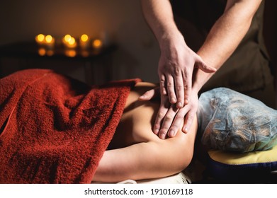 Male Strong Hands Massage Back To Middle Aged Woman In Dark Spa Room By Candlelight