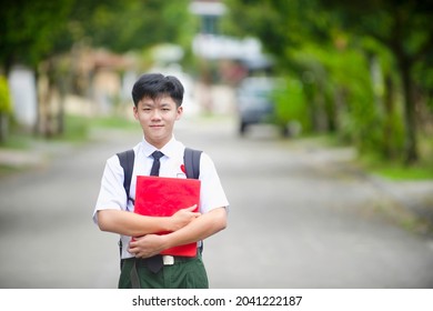 Male Student Carrying Backpack And Book In The Outdoor.Back To School Malaysian Child.Secondary Student Portrait In Malaysia.Education In Asia.Chinese Boy Wearing Uniform.Smiling Kid.