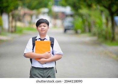 Male Student Carrying Backpack And Book In The Outdoor.Back To School Malaysian Child.Secondary Student Portrait In Malaysia.Education In Asia.Chinese Boy Wearing Uniform.Smiling Kid.