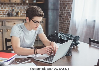 male student doing homework and typing on laptop at home