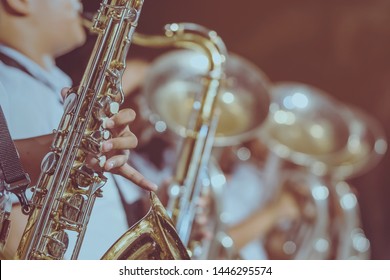 Male Student With Friends Blow The Saxophone With The Band For Performance On Stage At Night.