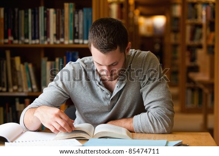 Male student researching with a book in a library