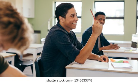 Male Student Sitting In The Class And Raising Hand Up To Ask Question During Lecture. High School Student Raises Hand And Asks Lecturer A Question.