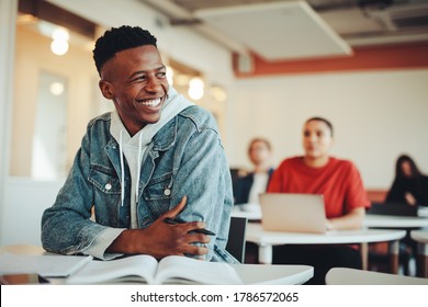 Male student sitting in university classroom looking away and smiling. Man sitting in lecture in high school classroom.