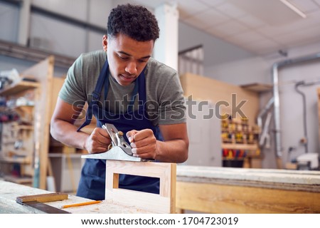 Male Student Studying For Carpentry Apprenticeship At College Using Wood Plane