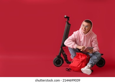 Male student with tablet computer, backpack and electric bike on red background