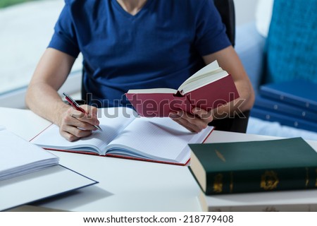 Male student transcribing the notes from the book in library