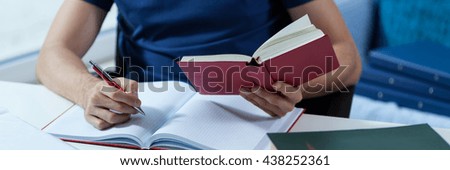 Male student transcribing the notes from the book in library