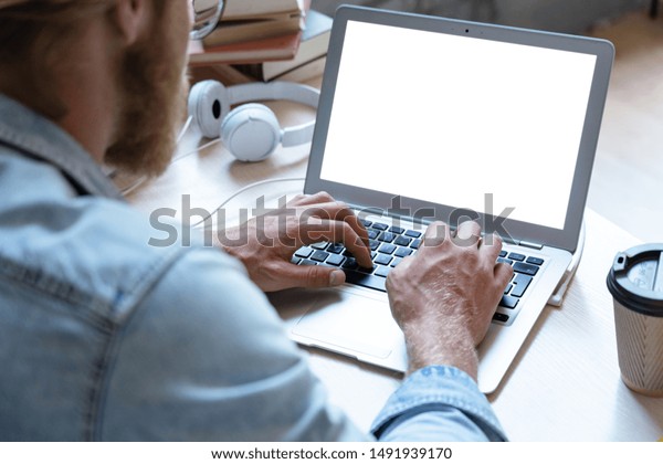 Male student using laptop software looking at empty\
white mock up computer screen learn easy internet course study\
online e learning in app type on notebook at table, over shoulder\
close up view