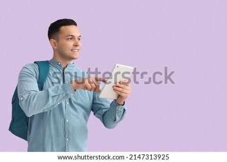 Male student using tablet computer on lilac background
