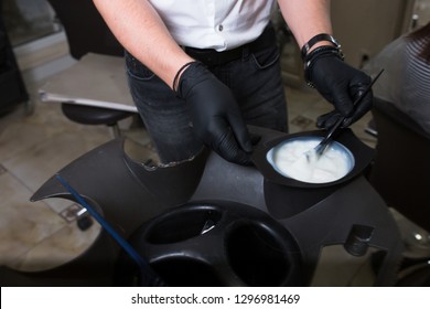 Male Stylist In Gloves Preparing Color Cream For Dying Hairin  A Container, A Mask For Treatment Procedure In Beauty Salon. Hhairdresser Mixing Brush Coloring Hair Concept Supplies. Spa Copy Space