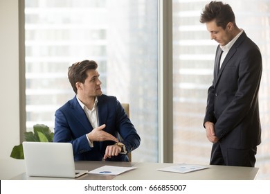 Male subordinate receiving reprimand from boss for being too late at meeting, company director scolding unpunctual manager for missing deadline or not finishing work on time, pointing on wristwatch 