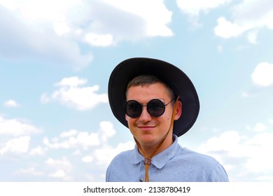 Male In Sunglasses. Portrait Of Farmer With Blue Sky In Background. Young Man Wearing Sunglasses And Cowboy Hat In Field. Closeup. Happy Young Person.