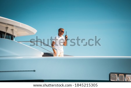 Male superyacht Deckhand with a handheld radio getting ready to drop anchor, with a blue sky in the background