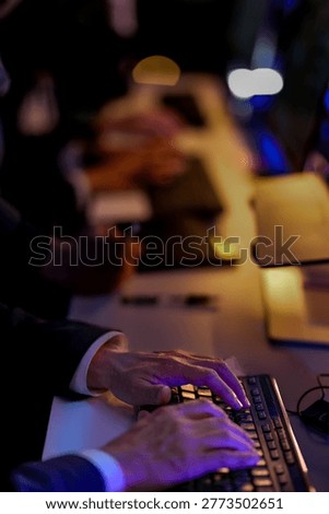 Male IT support agent using digital tablet and writing notes during overtime. Close up of corporate employee hands working on computer desk in a dark modern workplace.