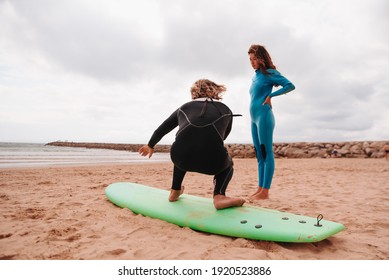 Male Surf Teacher Teaching A Young Latin Woman To Surf On The Beach