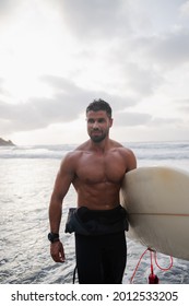 Male Surfer Holding Surf Board At The Beach At Sunset, He Is Young - Smiling Attractive Man Having Fun And Doing Extreme Sport - Happiness Of Millennials Concept - Focus On His Face