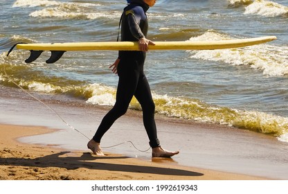 Male Surfer Looking At Camera. Full Length View Of Middle Aged Man In Wetsuit Holding Surfboard And Walking On Sandy Sea Coast. Surfing Concept. No Face