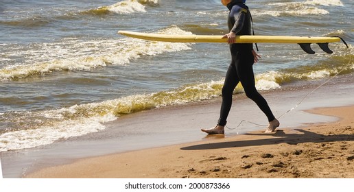 Male Surfer Looking At Camera. Full Length View Of Middle Aged Man In Wetsuit Holding Surfboard And Walking On Sandy Sea Coast. Surfing Concept. No Face