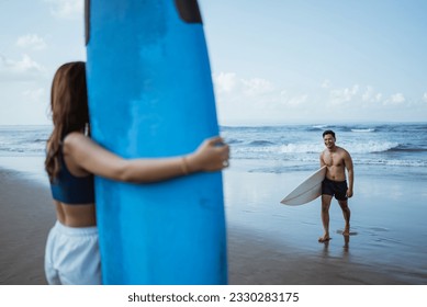 male surfer meets female friend with after practicing carrying surfboard on the beach - Powered by Shutterstock