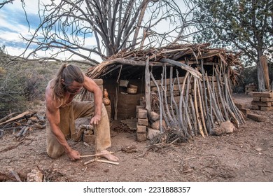 Male survivalist makes friction fire in front of simple shelter in mountains - Powered by Shutterstock