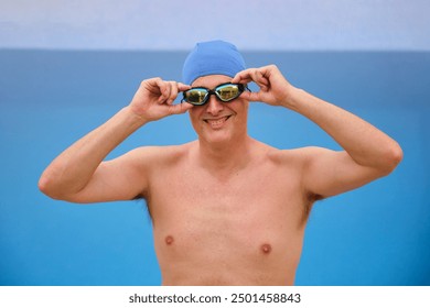 Male swimmer is adjusting his swimming goggles and smiling before diving into the pool - Powered by Shutterstock