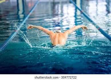 Male swimmer performing the butterfly stroke at indoor swimming competition