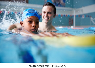 Male Swimming Coach Giving Boy Holding Float One To One Lesson In Pool