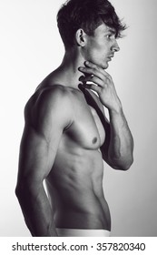 Male swimwear & underwear concept. Handsome muscular male model in trendy white underwear posing over grey background. Studio shot