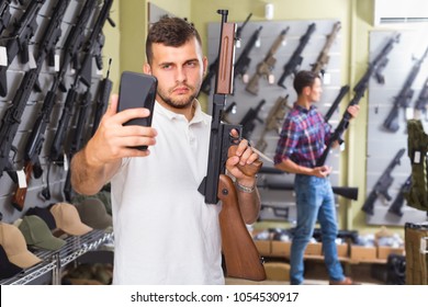 Male is taking selfie on phone with air gun in airsoft shop.  - Shutterstock ID 1054530917