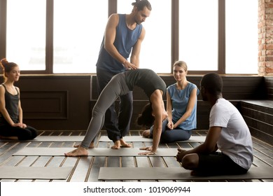 Male teacher assisting young woman doing yoga exercise on mat, instructor helping flexible girl performing bridge pose, urdhva dhanurasana or chakrasana at group training class with diverse people - Powered by Shutterstock