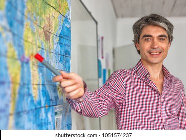 Male teacher in the classroom teaching geography pointing to a world map. - Powered by Shutterstock