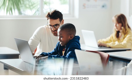 Male teacher helps a young boy with computer-based learning in a classroom setting. Child tutor providing a lesson in an elementary school, with a focus on coding and basic digital literacy.
