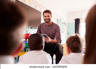 Male Teacher Holding Digital Tablet Teaches Group Of Uniformed Elementary Pupils In School Classroom