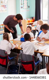 Male Teacher Holding Digital Tablet Teaches Group Of Uniformed Elementary Pupils In School Classroom