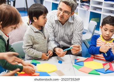 A male teacher, interacts with young children, Asian and Hispanic, in a classroom. The teacher and children are engaged in a classroom activity. Diverse kids at elementary school with teacher. - Powered by Shutterstock