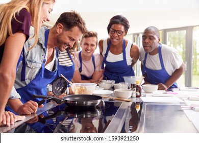 Male Teacher Making Pancake On Cooker In Cookery Class As Adult Students Look On