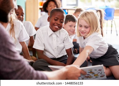 Male Teacher Reading Story To Group Of Elementary Pupils Wearing Uniform In School Classroom - Shutterstock ID 1448056133