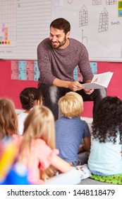 Male Teacher Reading Story To Group Of Elementary Pupils In School Classroom