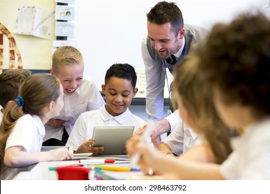 A male teacher sits supervising a group of children who are working on whiteboards and digital tablets.  - Powered by Shutterstock