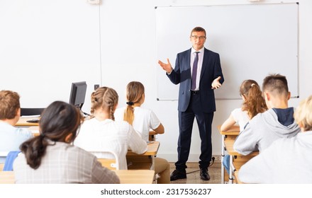 Male teacher standing at whiteboard in classroom, conducting lesson with teen students - Powered by Shutterstock