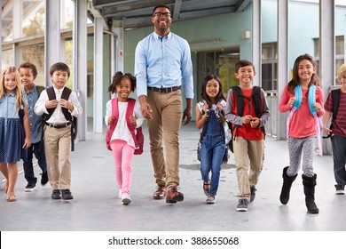 Male Teacher Walking In Corridor With Elementary School Kids