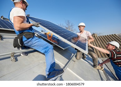 Männliche Team-Ingenieure installieren eigenständige Solarzellenanlage. Elektrische Hebezeuge mit blauem Solarmodul auf dem Dach des modernen Hauses. Alternatives ökologisches Energiekonzept.