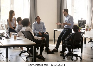 Male team leader boss talking to diverse business people at office meeting, multiracial employees group listening to ceo mentor coach speaking explaining new idea at corporate training or briefing