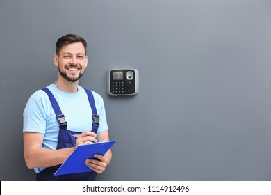 Male Technician With Clipboard Near Installed Alarm System Indoors