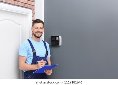 Male technician with clipboard near installed alarm system indoors